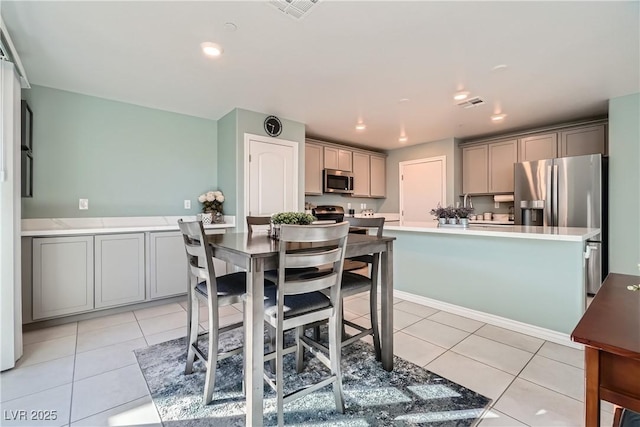 kitchen with light tile patterned floors, appliances with stainless steel finishes, gray cabinets, and a kitchen island