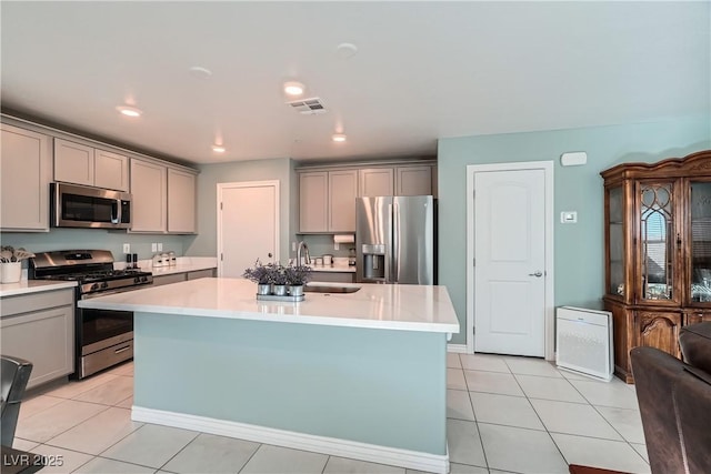 kitchen featuring light tile patterned flooring, a center island with sink, stainless steel appliances, and gray cabinetry