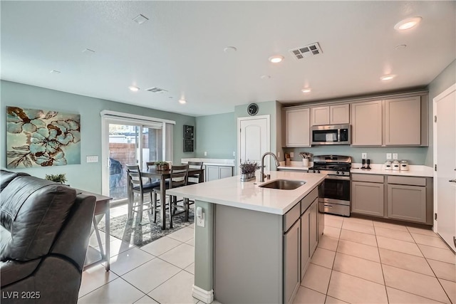 kitchen with sink, appliances with stainless steel finishes, gray cabinetry, and a kitchen island with sink