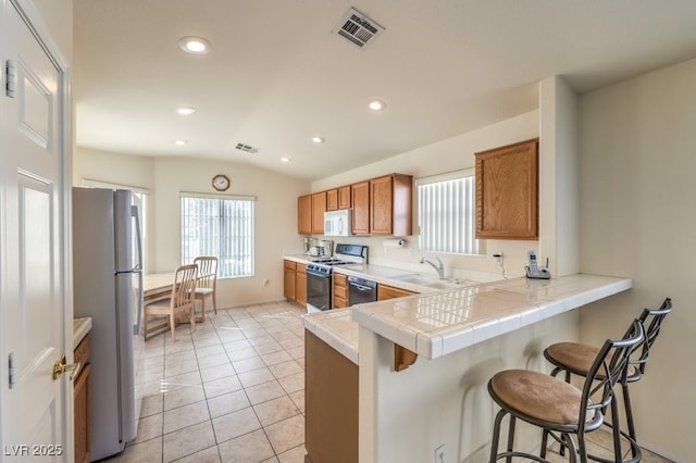 kitchen with sink, range with gas cooktop, kitchen peninsula, tile countertops, and fridge