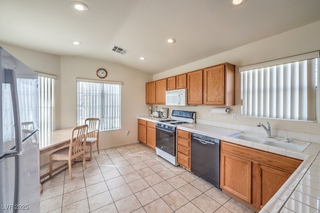 kitchen featuring vaulted ceiling, tile counters, white appliances, and sink