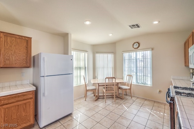 kitchen with tile counters, light tile patterned floors, and white appliances