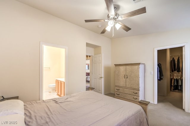 bedroom with a walk in closet, ensuite bathroom, light colored carpet, ceiling fan, and a closet