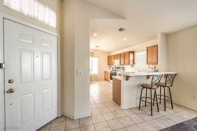 kitchen with a kitchen bar, kitchen peninsula, gas range oven, sink, and light tile patterned flooring