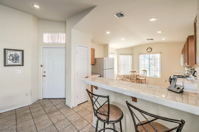 kitchen with tile countertops, lofted ceiling, white appliances, a breakfast bar area, and light tile patterned floors