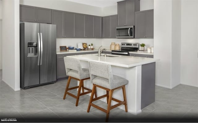 kitchen featuring sink, stainless steel appliances, a kitchen island with sink, a breakfast bar, and light tile patterned floors