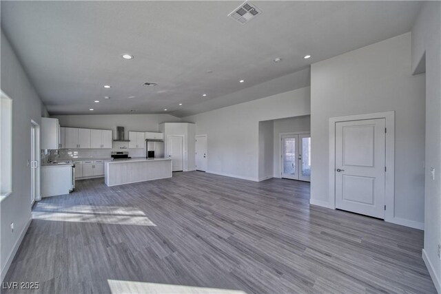 unfurnished living room featuring french doors, vaulted ceiling, and light wood-type flooring