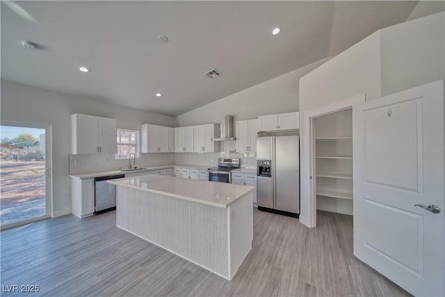 kitchen with a center island, white cabinets, wall chimney range hood, sink, and stainless steel appliances