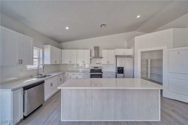 kitchen featuring wall chimney exhaust hood, stainless steel appliances, sink, white cabinets, and a kitchen island