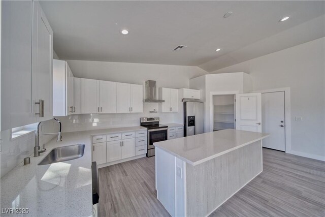 kitchen with sink, wall chimney exhaust hood, vaulted ceiling, white cabinets, and appliances with stainless steel finishes