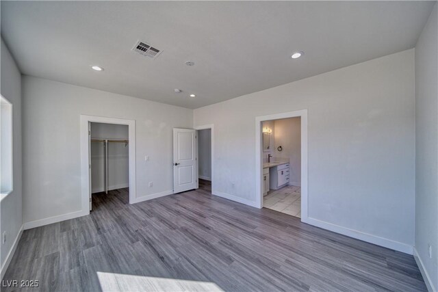 unfurnished bedroom with light hardwood / wood-style flooring, a spacious closet, a closet, and ensuite bathroom