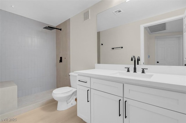 bathroom featuring tiled shower, vanity, hardwood / wood-style flooring, and toilet