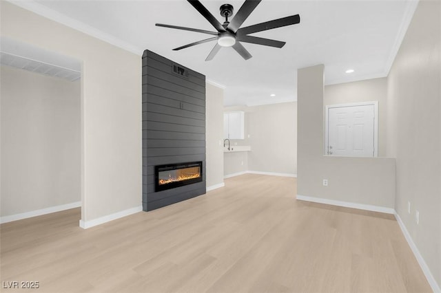 unfurnished living room featuring ornamental molding, ceiling fan, sink, a fireplace, and light hardwood / wood-style floors