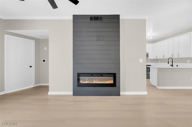 unfurnished living room featuring ornamental molding, a large fireplace, ceiling fan, sink, and light hardwood / wood-style floors