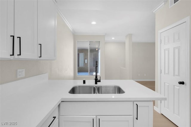 kitchen with kitchen peninsula, ornamental molding, sink, light hardwood / wood-style floors, and white cabinetry