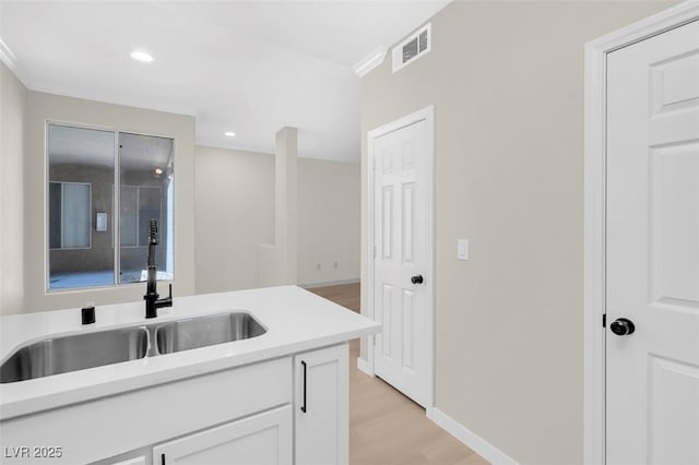 kitchen with sink, white cabinets, ornamental molding, and light hardwood / wood-style flooring