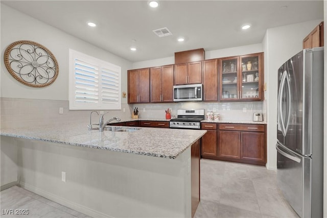 kitchen with stainless steel appliances, sink, tasteful backsplash, kitchen peninsula, and light stone countertops