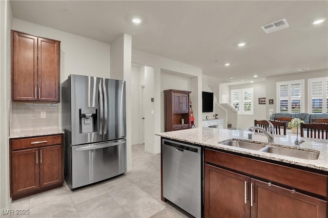 kitchen featuring light stone counters, stainless steel appliances, decorative backsplash, and sink