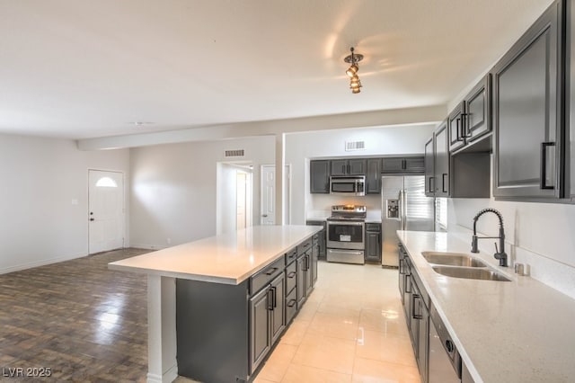 kitchen with sink, a kitchen island, light tile patterned floors, and appliances with stainless steel finishes