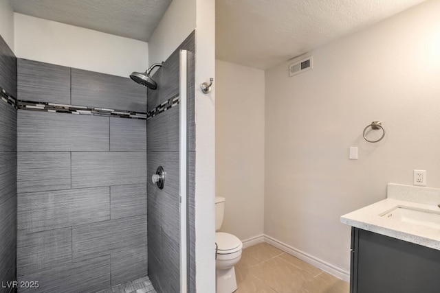 bathroom featuring tile patterned flooring, a textured ceiling, tiled shower, toilet, and vanity