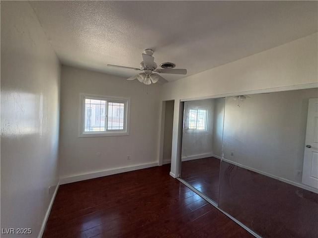 unfurnished bedroom featuring dark hardwood / wood-style flooring, multiple windows, a closet, and ceiling fan