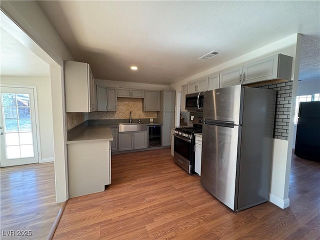 kitchen with appliances with stainless steel finishes, sink, wood-type flooring, gray cabinets, and wine cooler