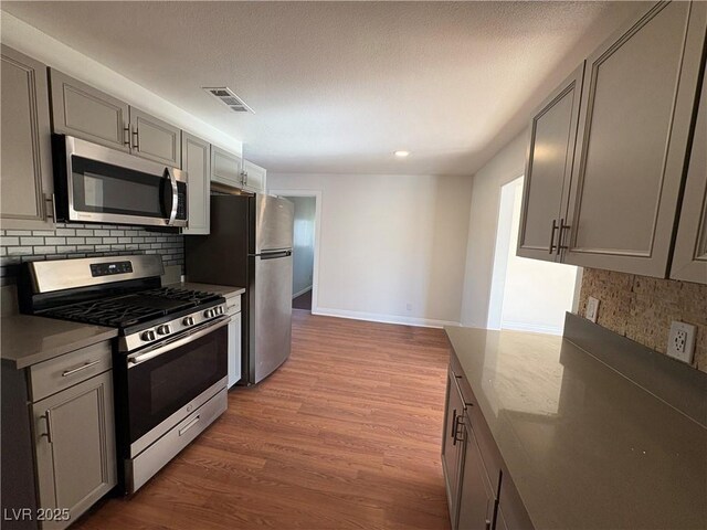 kitchen with gray cabinetry, decorative backsplash, and appliances with stainless steel finishes