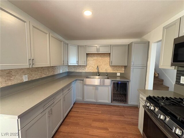 kitchen featuring gray cabinetry, stainless steel appliances, beverage cooler, sink, and light hardwood / wood-style flooring