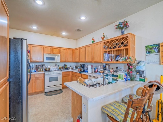 kitchen featuring white appliances, kitchen peninsula, sink, and a breakfast bar area