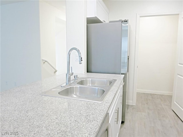 kitchen featuring light stone countertops, sink, white cabinets, and light hardwood / wood-style flooring