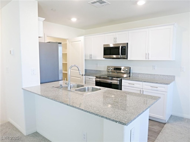 kitchen featuring kitchen peninsula, light stone countertops, stainless steel appliances, sink, and white cabinets