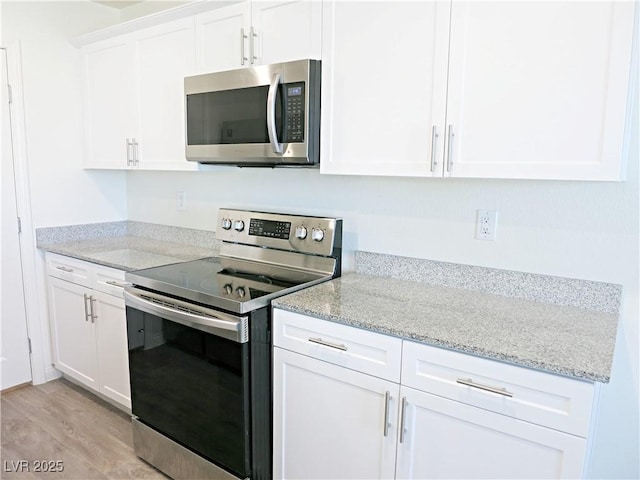 kitchen with light hardwood / wood-style floors, light stone countertops, white cabinetry, and appliances with stainless steel finishes