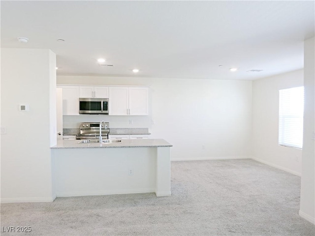 kitchen with light stone countertops, appliances with stainless steel finishes, light colored carpet, sink, and white cabinetry