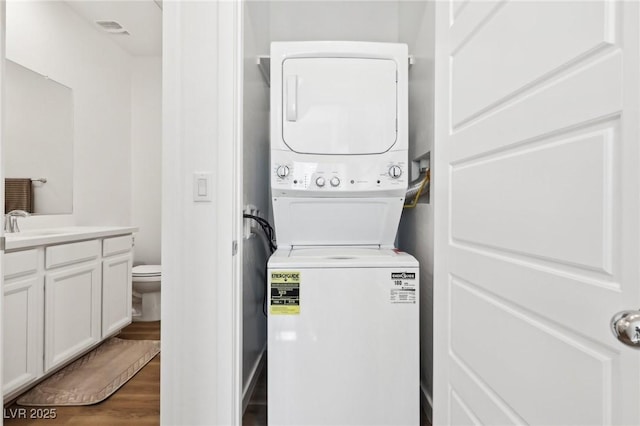 laundry area with stacked washing maching and dryer, sink, and dark wood-type flooring