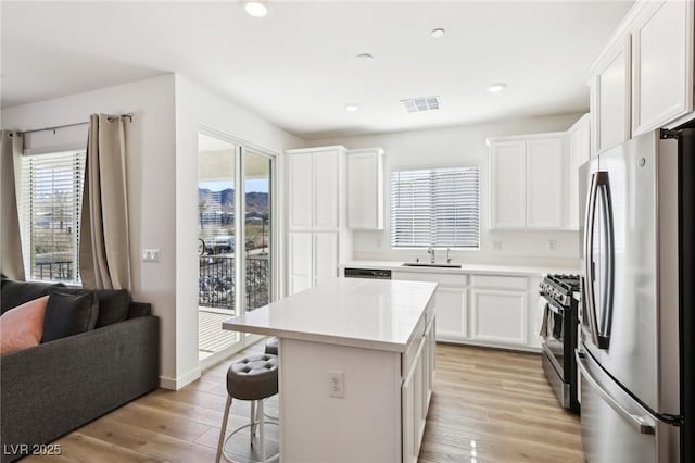 kitchen featuring white cabinetry, stainless steel appliances, light hardwood / wood-style flooring, a kitchen bar, and a kitchen island