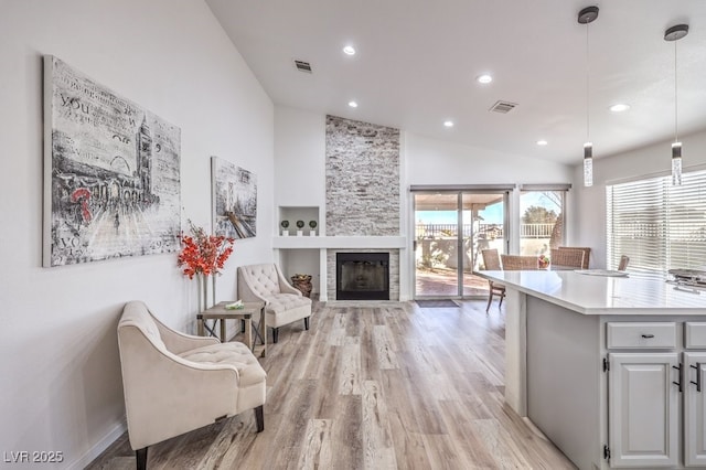 kitchen with white cabinets, vaulted ceiling, light hardwood / wood-style floors, hanging light fixtures, and a stone fireplace