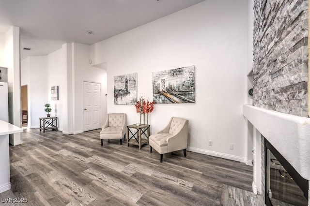 sitting room with a high ceiling, dark hardwood / wood-style flooring, and a stone fireplace