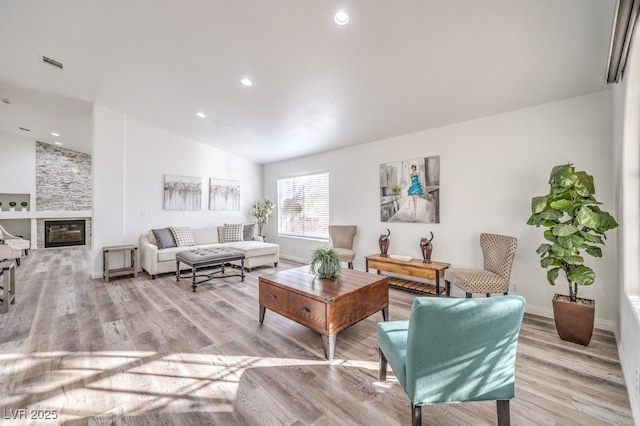 living room featuring a fireplace, light wood-type flooring, and vaulted ceiling