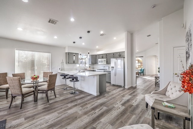 kitchen featuring white appliances, kitchen peninsula, dark hardwood / wood-style floors, gray cabinetry, and a breakfast bar area