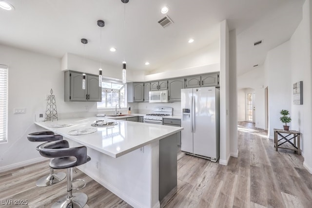 kitchen featuring sink, white appliances, a kitchen bar, kitchen peninsula, and pendant lighting