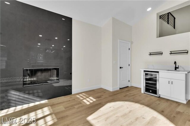 bar with sink, beverage cooler, a fireplace, white cabinets, and light wood-type flooring