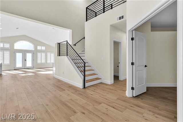 foyer with light hardwood / wood-style floors, high vaulted ceiling, and french doors