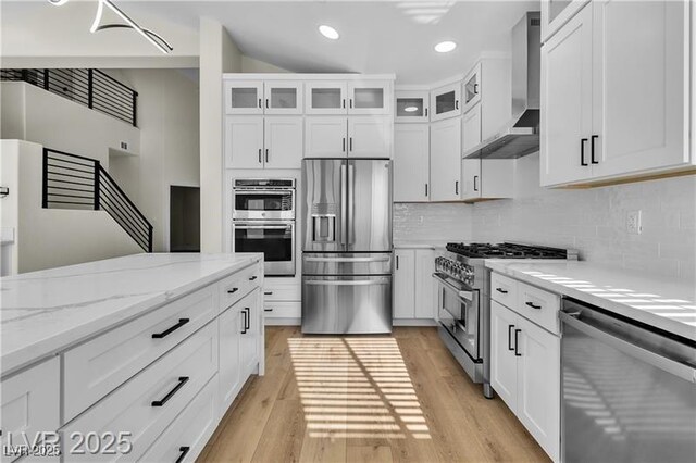 kitchen with appliances with stainless steel finishes, white cabinetry, and wall chimney exhaust hood