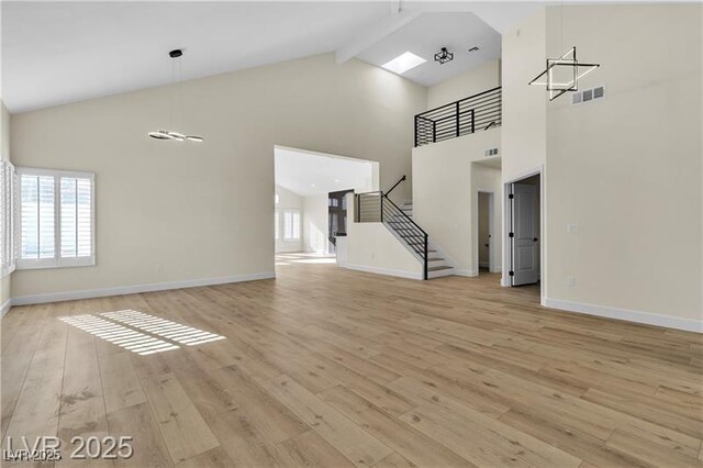 unfurnished living room featuring beam ceiling, high vaulted ceiling, and light wood-type flooring