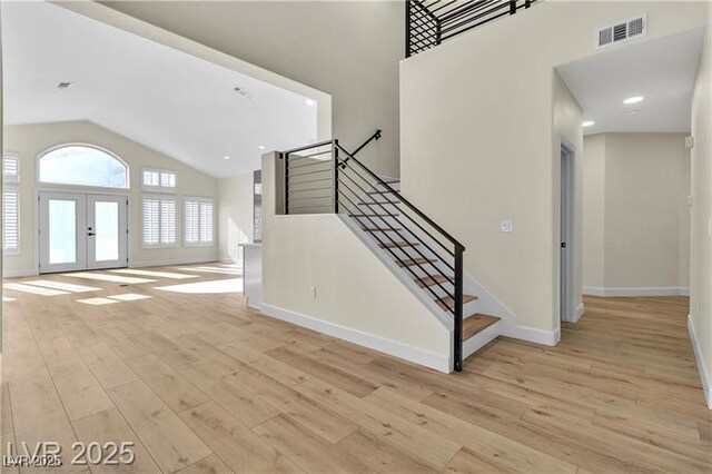 foyer entrance with french doors, light hardwood / wood-style floors, and high vaulted ceiling