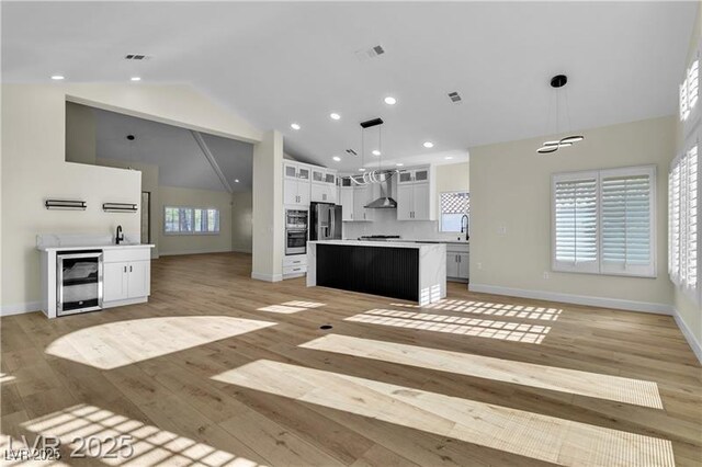 kitchen featuring wall chimney range hood, a kitchen island, vaulted ceiling, decorative light fixtures, and white cabinets