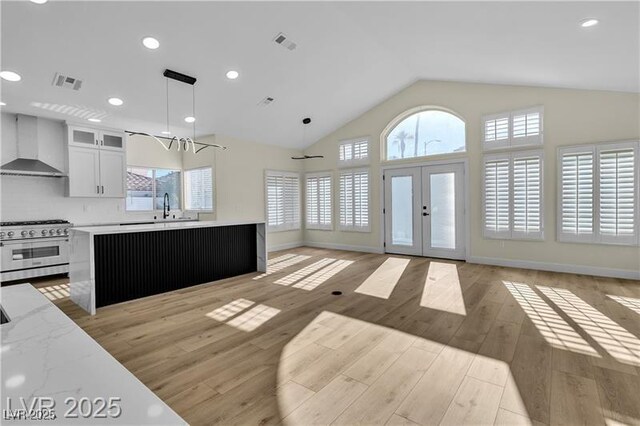 kitchen featuring wall chimney exhaust hood, hanging light fixtures, light hardwood / wood-style floors, high end stainless steel range, and white cabinets