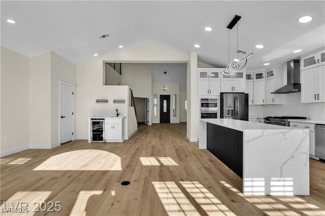 kitchen featuring backsplash, wall chimney range hood, appliances with stainless steel finishes, a kitchen island, and white cabinetry