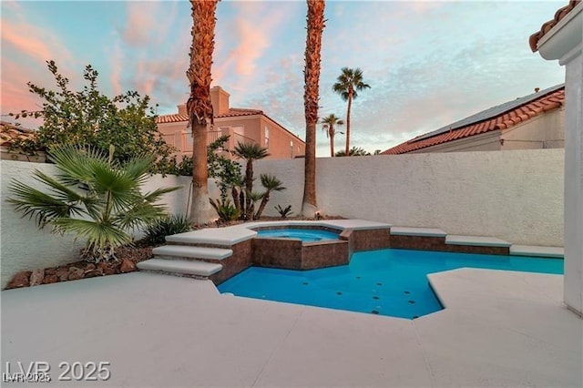 pool at dusk featuring a patio area and an in ground hot tub