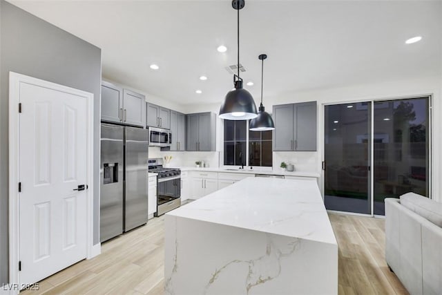 kitchen with light stone counters, gray cabinetry, stainless steel appliances, decorative light fixtures, and a center island